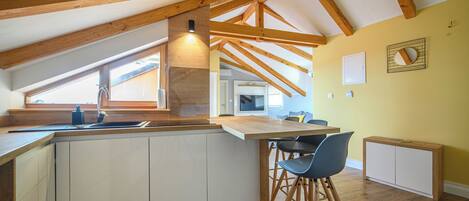 A kitchen with wooden beams, a large window, and a bar area with stools.