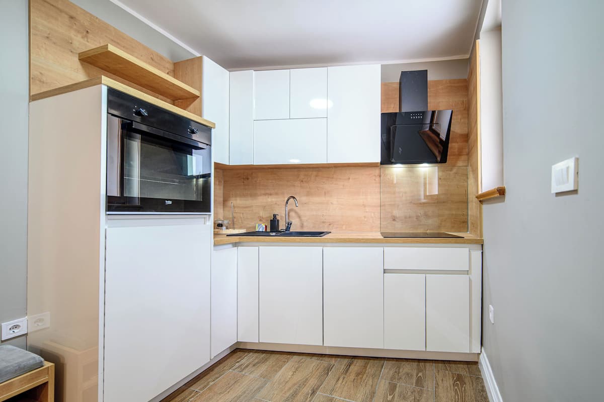 A compact kitchen with white cabinets, a black oven, and a wooden countertop.