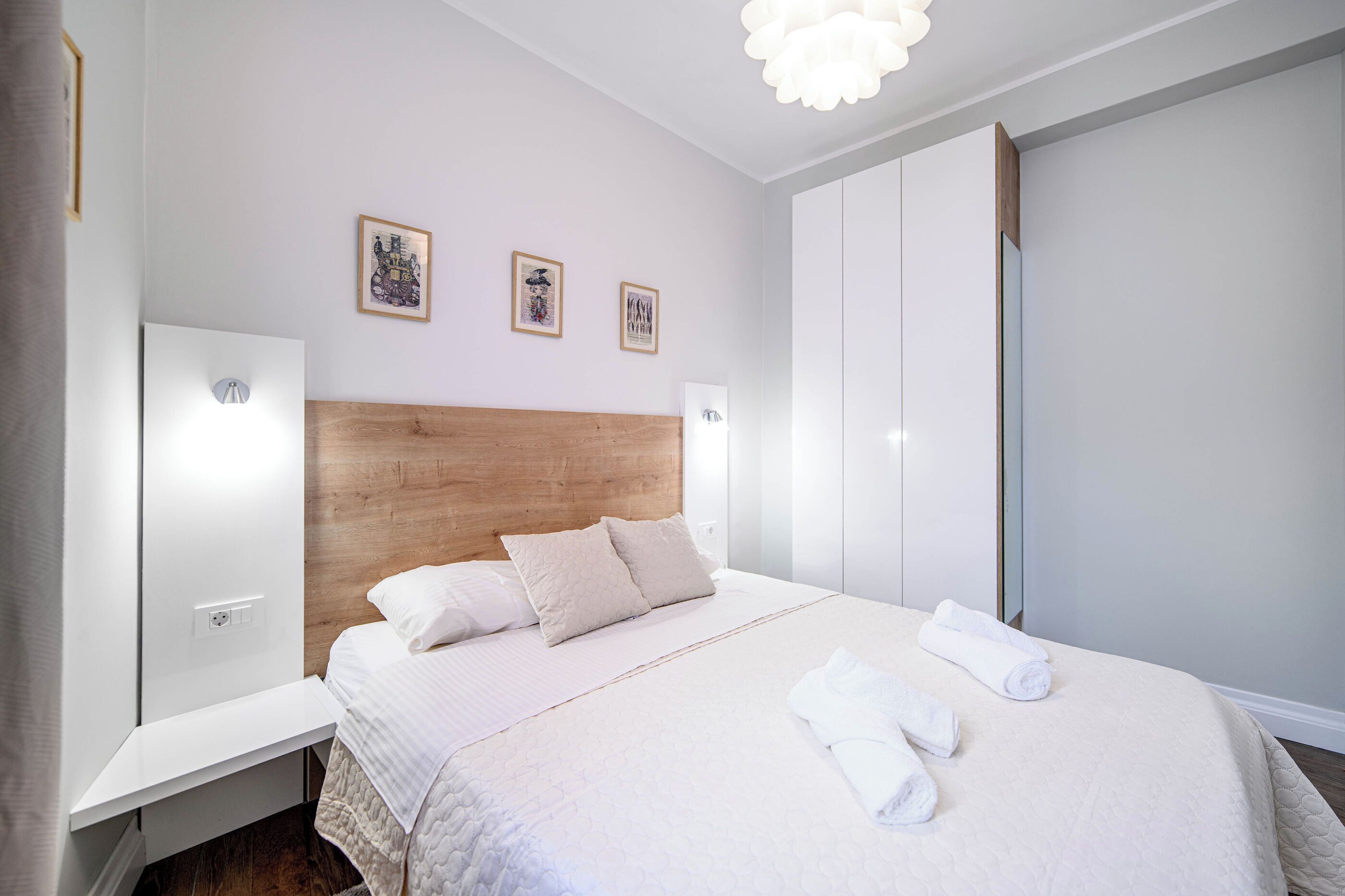 Ein ordentlich eingerichtetes Schlafzimmer mit einem Holz-Kopfteil, einem weißen Bett mit Tagesdecke und zwei Nachttischen.