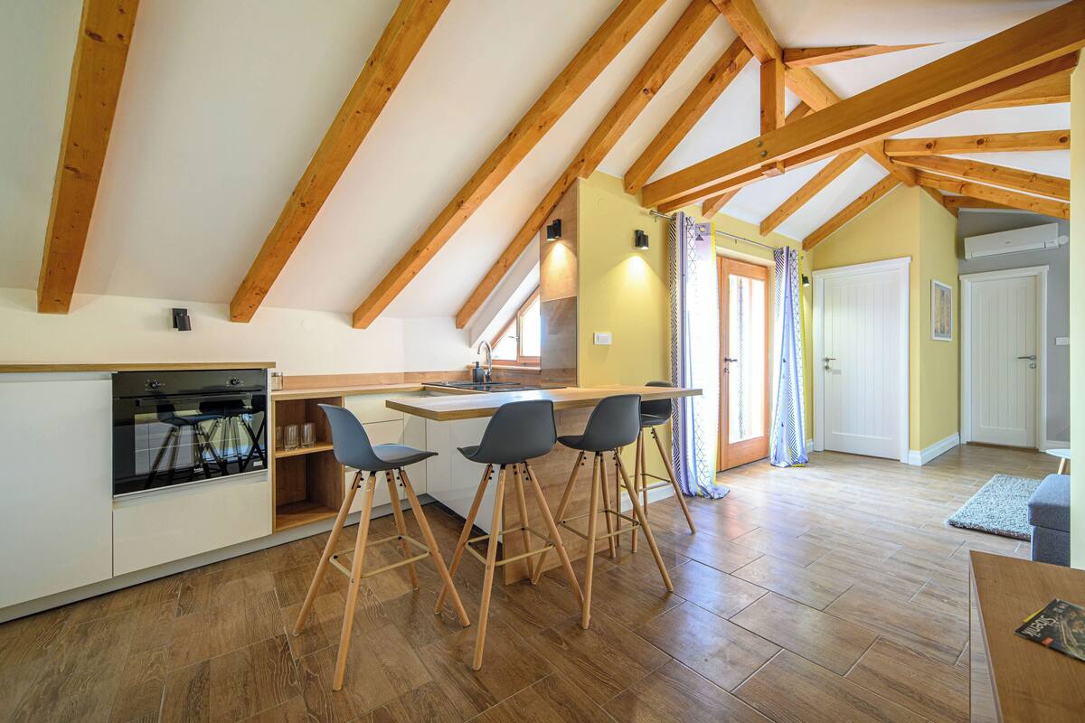 A kitchen with wooden beams, a built-in oven, and bar stools.