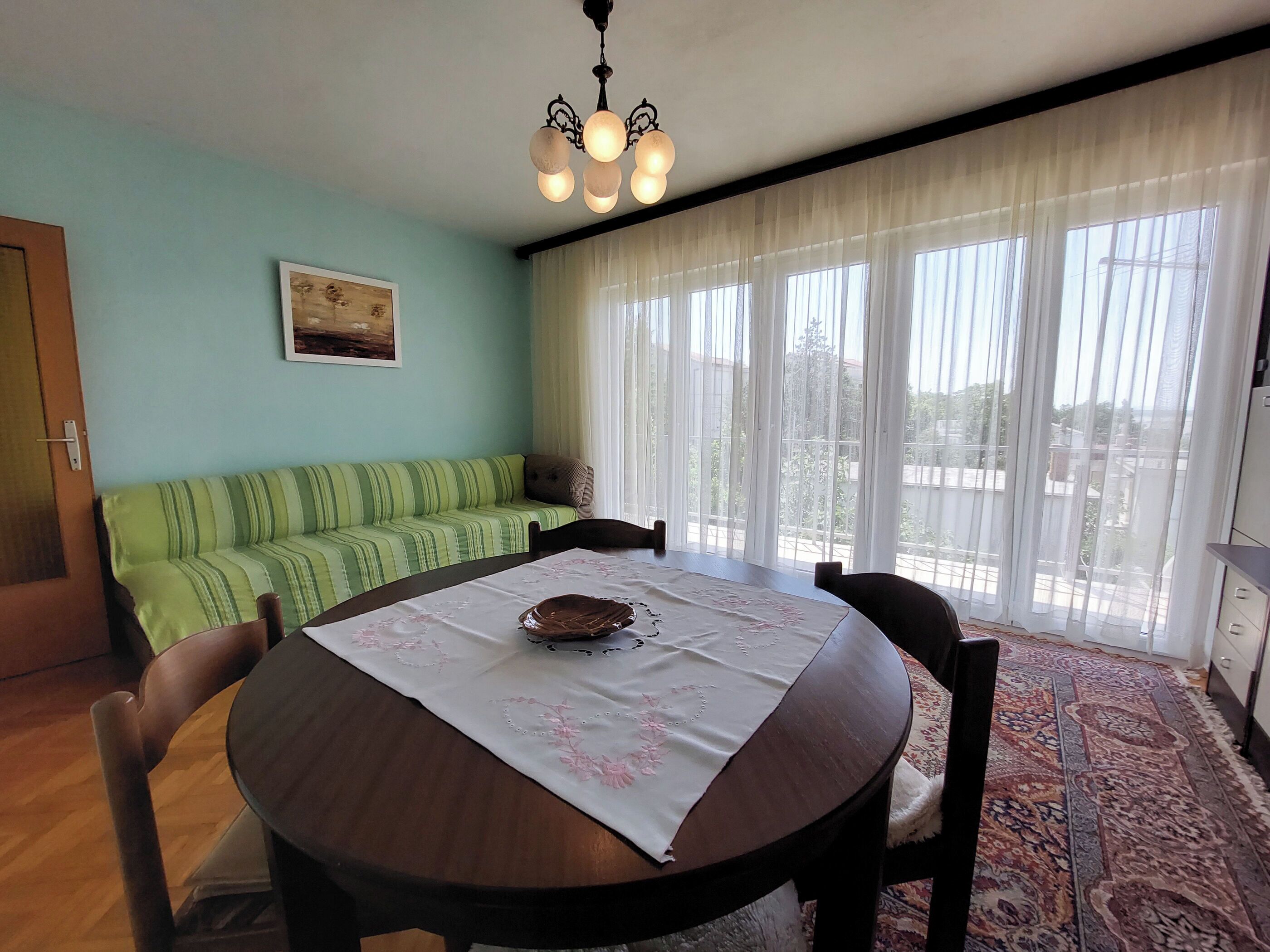 A dining area with a round table, chairs, a green sofa, and a chandelier.