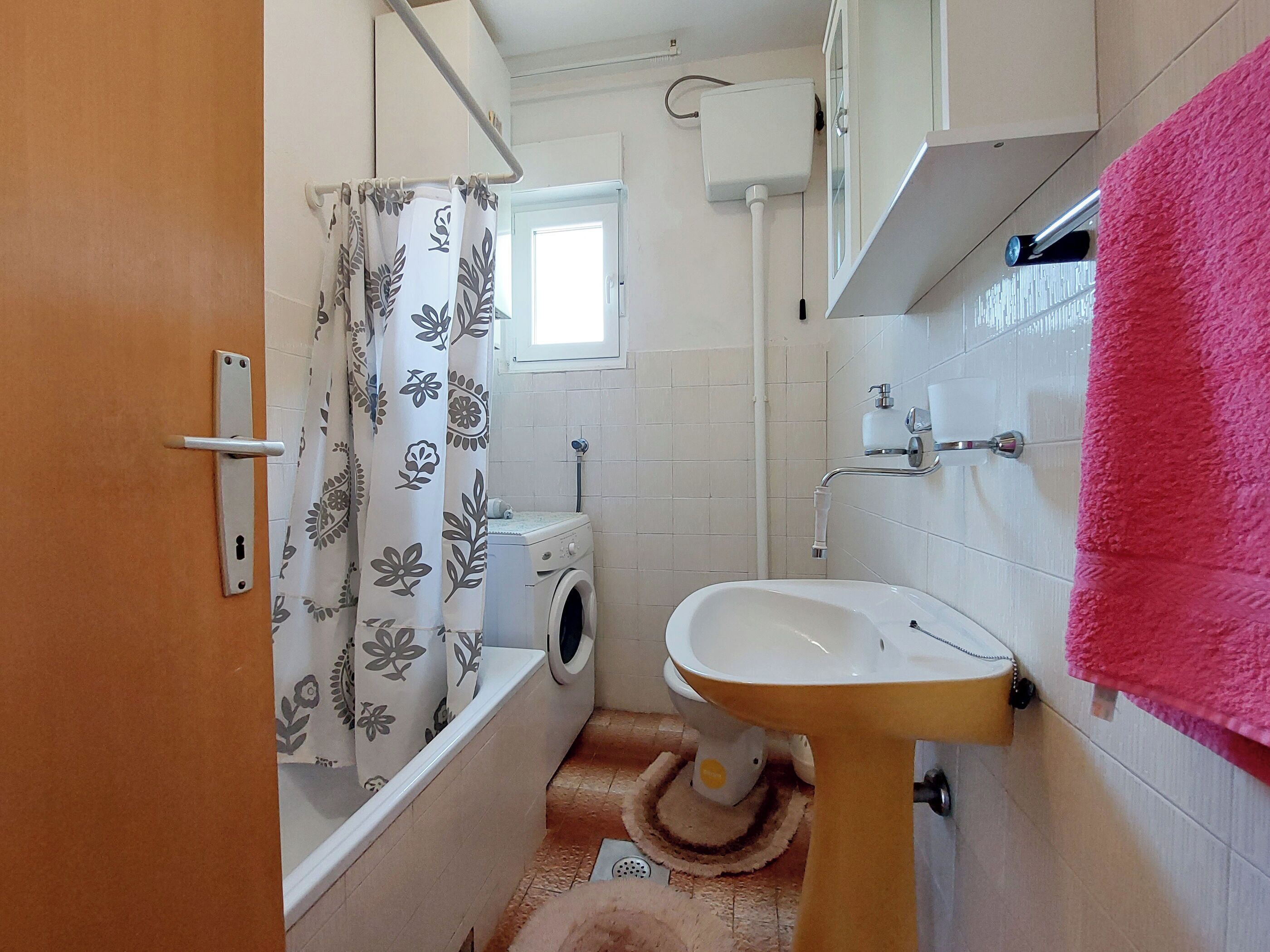 A bathroom with a toilet, washing machine, sink, and a shower curtain.