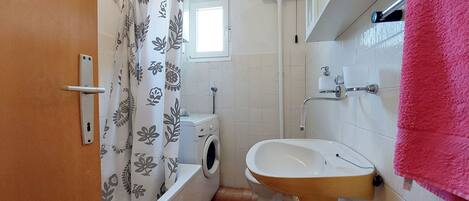 A bathroom with a toilet, washing machine, sink, and a shower curtain.