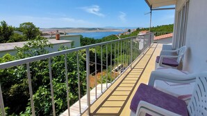 En balkon med havudsigt, gelænder og en række hvide stole med lilla puder.