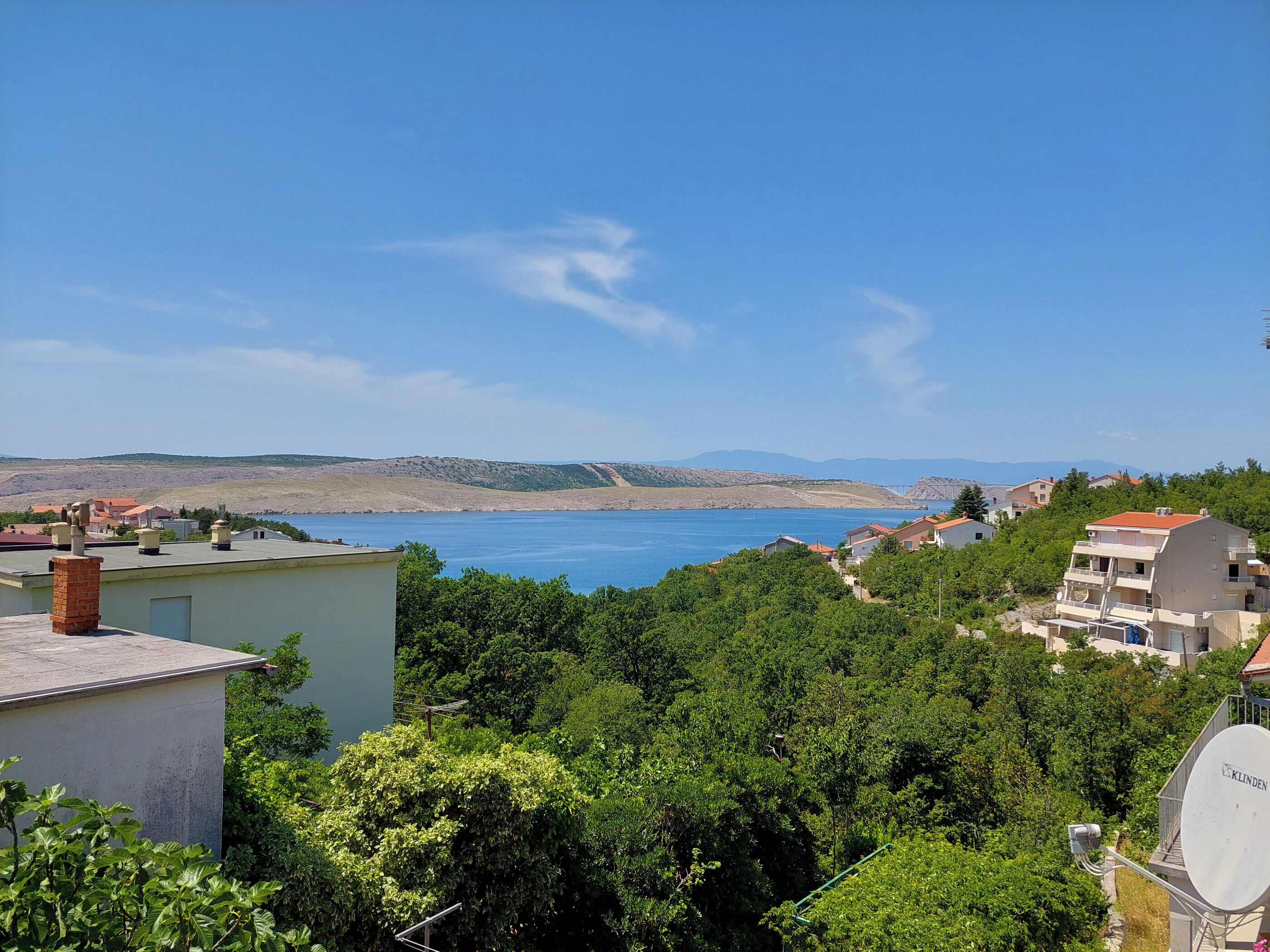 Ein Küstenwohngebiet mit Häusern, einer Satellitenschüssel und freiem Blick auf das Meer und die entfernten Hügel.