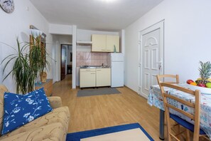 A compact living space with a kitchenette, a dining area with a table and chairs, and a sofa with a blue pillow. - Apartment Megi (Crikvenica)