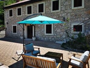 A stone building with a tiled patio, outdoor seating, and a blue umbrella. - House Nada Franciska (Vinodol)