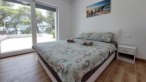 Una camera da letto con un letto grande, un comodino, un quadro e vista su un balcone esterno tramite un'ampia porta scorrevole.