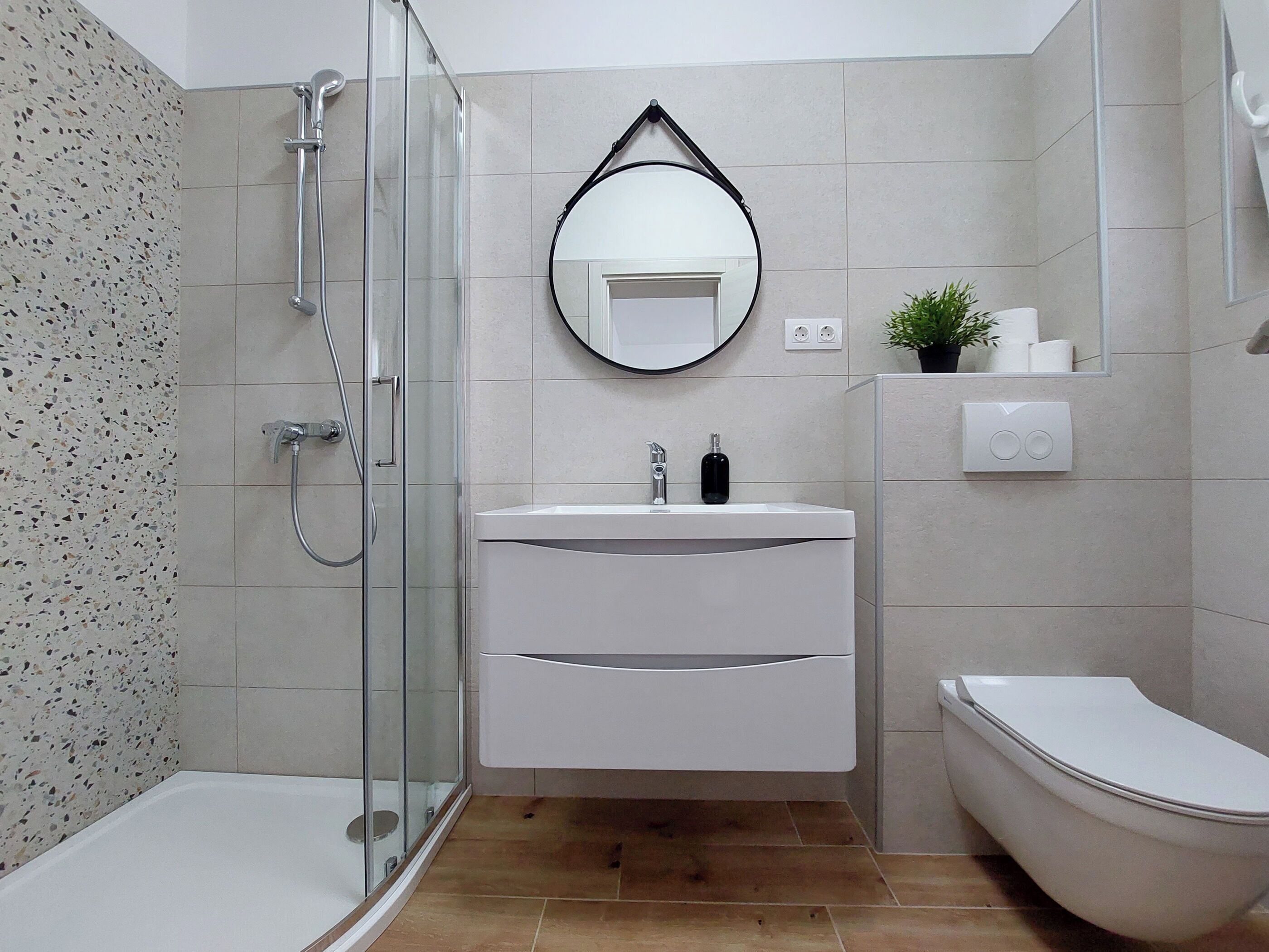 Une salle de bain moderne avec une douche à parois de verre, un lavabo blanc avec un miroir au-dessus et des toilettes.