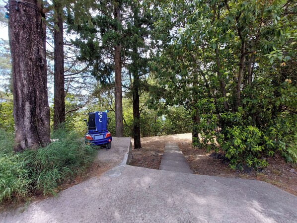 A paved path leading through a wooded area with a blue vehicle parked on the side. - Apartment and Rooms Anne (Crikvenica)