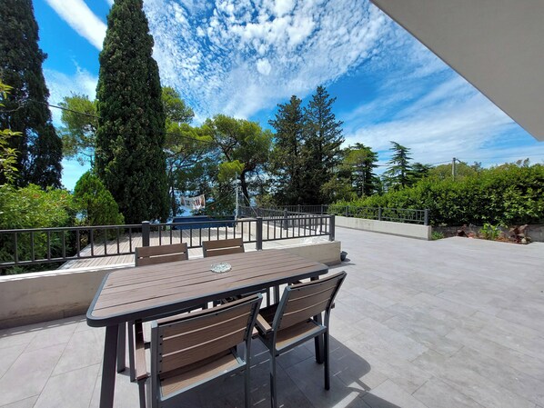 Une terrasse extérieure avec une table et des chaises, entourée de verdure et sous un ciel dégagé.