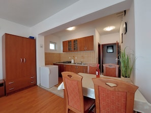 A compact kitchen with wooden cabinets, a refrigerator, a sink, and a dining area with chairs. - Apartments Irena (Crikvenica)