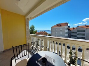 Un balcon avec une table et des chaises, donnant sur un paysage urbain avec des bâtiments et une étendue d’eau.