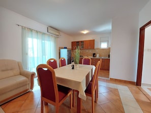 A dining area with a table, chairs, and a sofa. There is a kitchen in the background with cabinets and appliances. - Apartments Irena (Crikvenica)