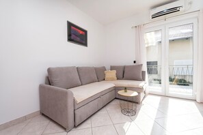 A modern living room with a beige sectional sofa, a small round side table, and a framed picture on the wall. - Apartments Ria Vodice (Vodice)