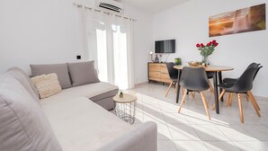 Un soggiorno moderno con un divano, un tavolo da pranzo con sedie, una TV a parete e un quadro sopra il tavolo.
