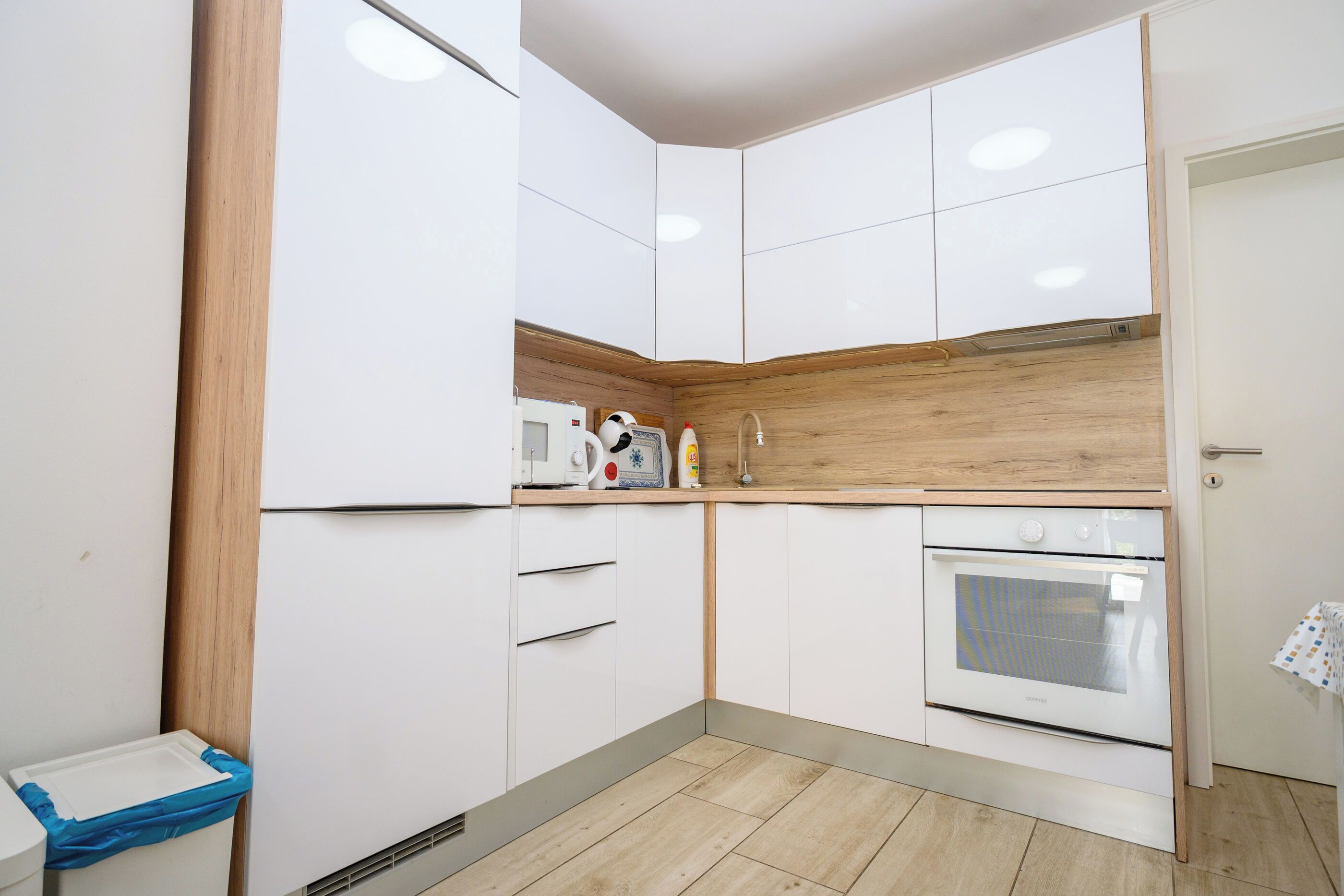 A compact kitchen with white cabinets, a wooden countertop, a built-in oven, and a small trash bin.