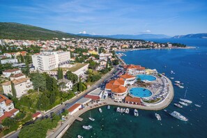 An aerial view of a coastal town with a prominent hotel, clear blue sea, and several boats docked near the waterfront. - Apartment Matej (Crikvenica)