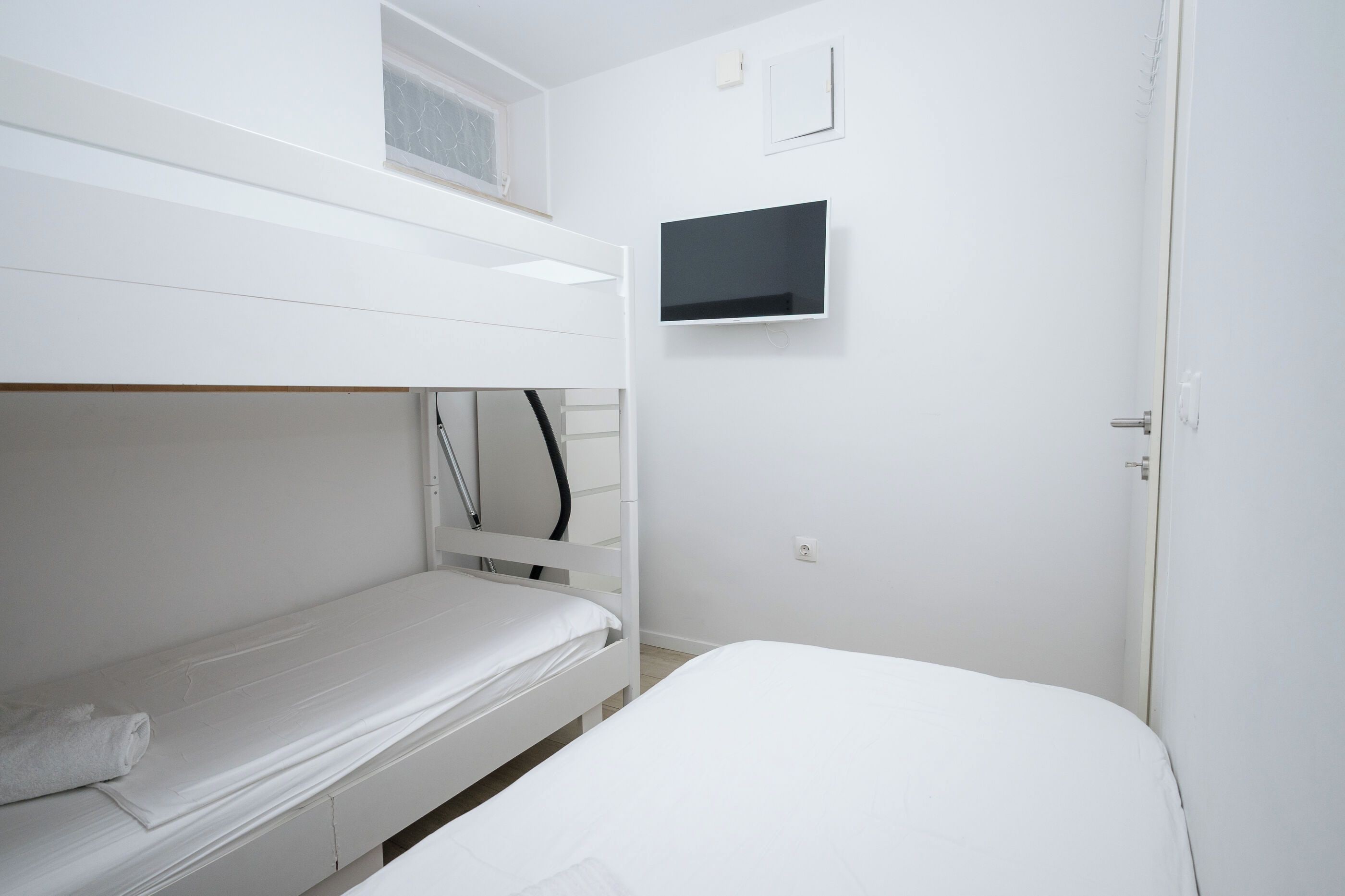 A bunk bed room with a television on the wall and a door.
