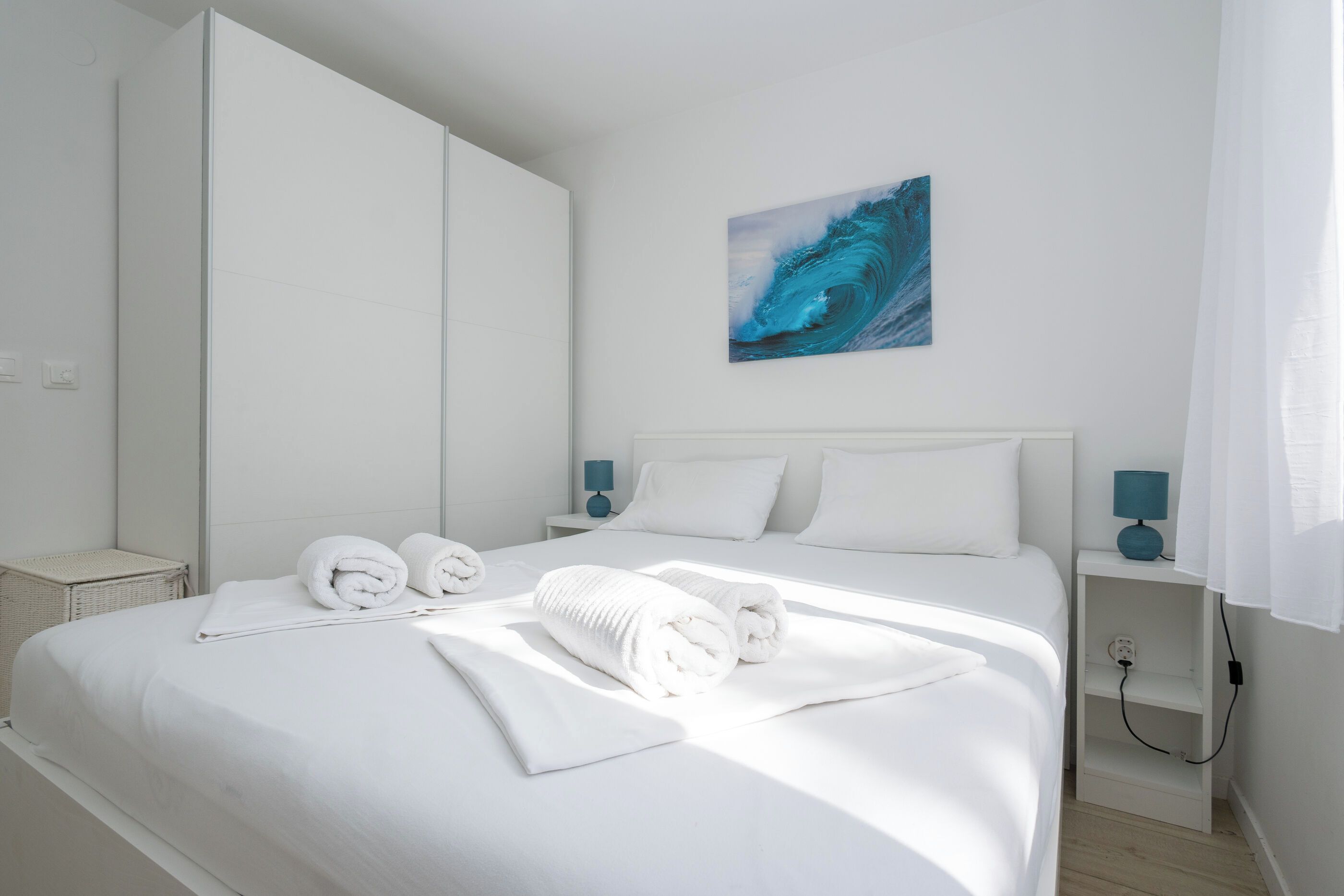 Una camera d'albergo con un letto grande, due comodini, un quadro appeso al muro e una presa di corrente.