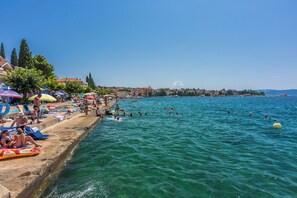 A beach with people swimming and sunbathing, a clear sky, and a distant view of a hill. - Apartment Matej (Crikvenica)