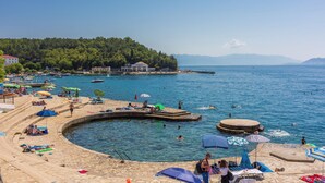 Eine Küstenlandschaft mit Schwimmbad, Liegestühlen, Sonnenschirmen und einem Steg.
