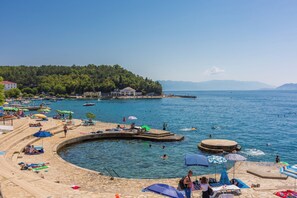 A coastal area with a swimming pool, beach chairs, umbrellas, and a pier. - Apartment Matej (Crikvenica)