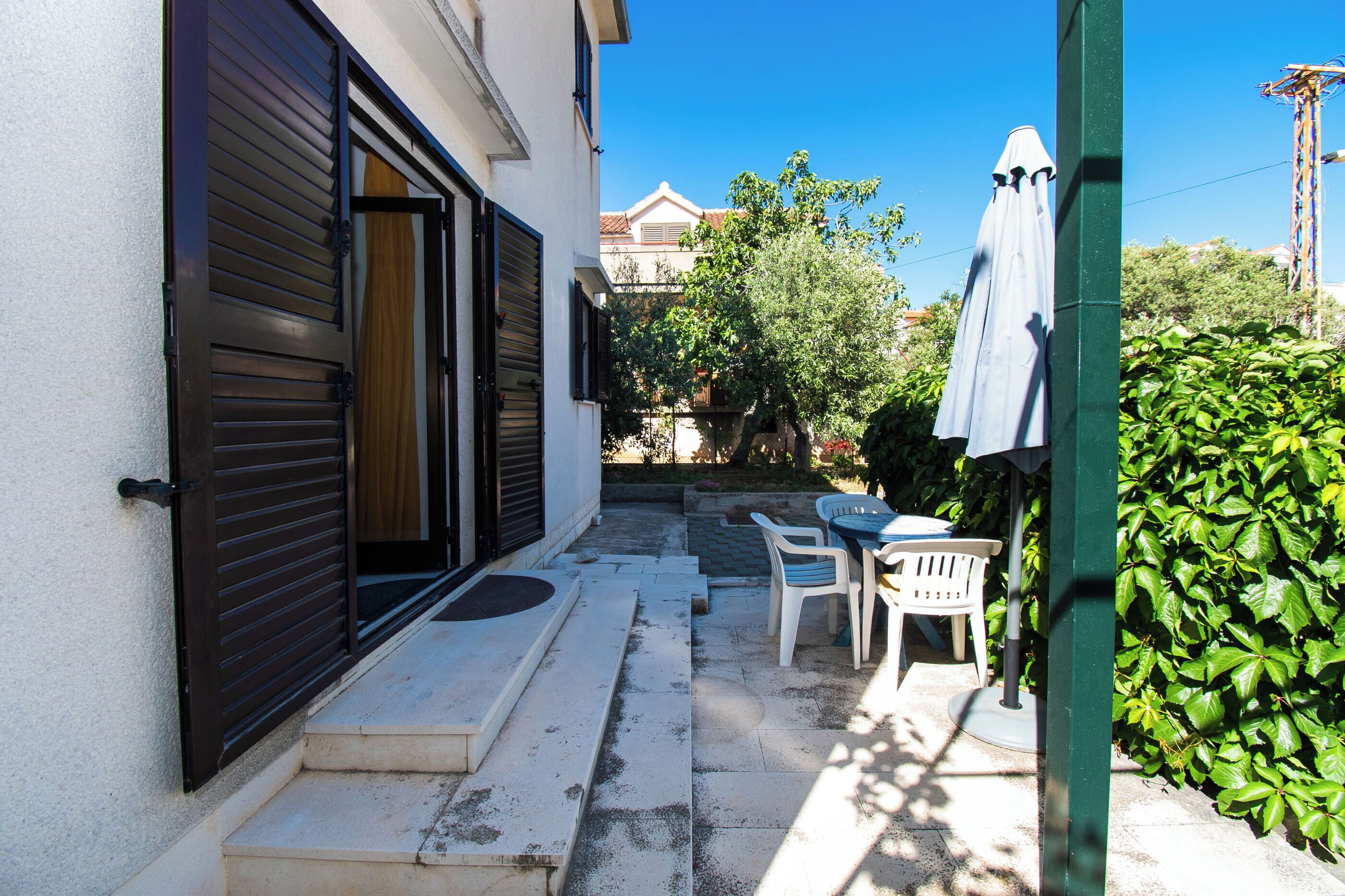 Un patio con una mesa y sillas blancas, una puerta de madera y un seto verde.