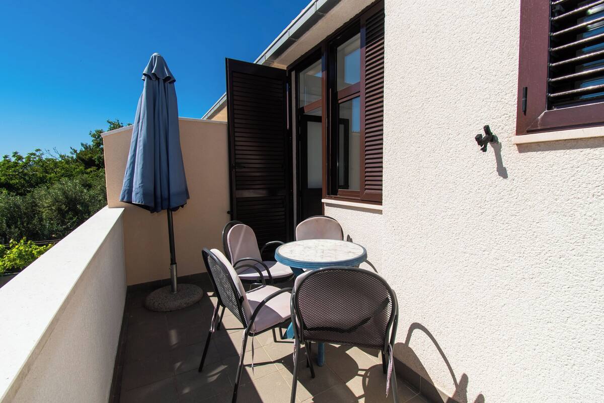 A balcony with a table and chairs, a blue umbrella, and a window with shutters.