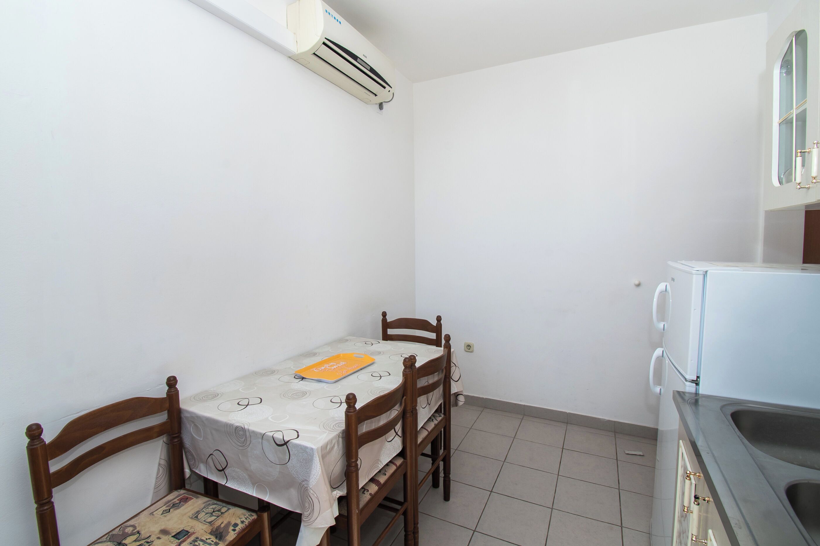 A small, clean kitchen with a table and chairs, a white air conditioner, and a sink.