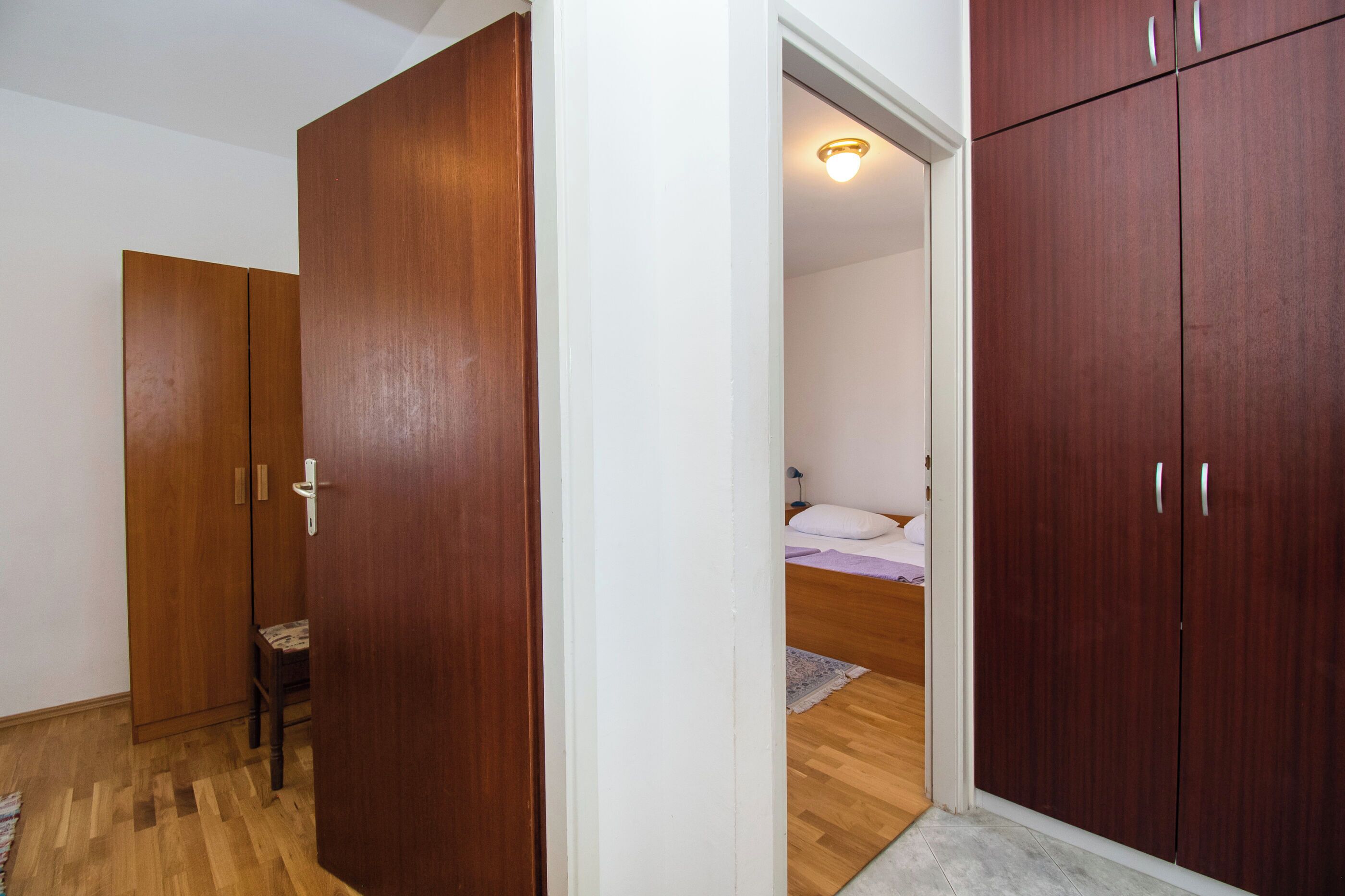 A bedroom with wooden wardrobes, a bed with a white headboard, and a small table.