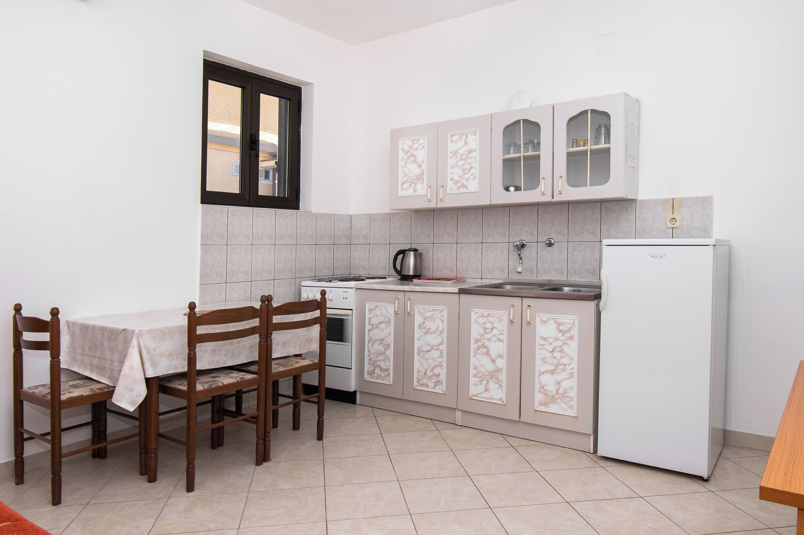 A compact kitchen with a dining table, chairs, a refrigerator, and cabinets.