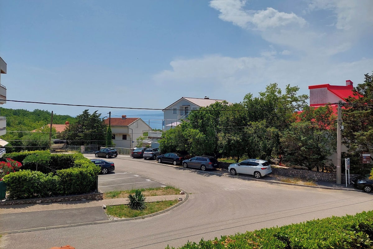 A residential street with parked cars, houses, and greenery.