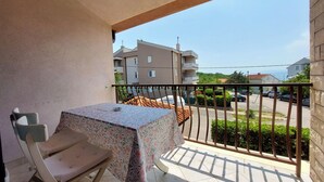 A balcony with a table and chair, a view of the street, and a building in the background. - Apartments Ilija (Crikvenica)
