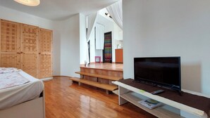 A modern room with a bed, wooden wardrobe, TV, and a staircase leading to another area. - Apartments Ilija (Crikvenica)