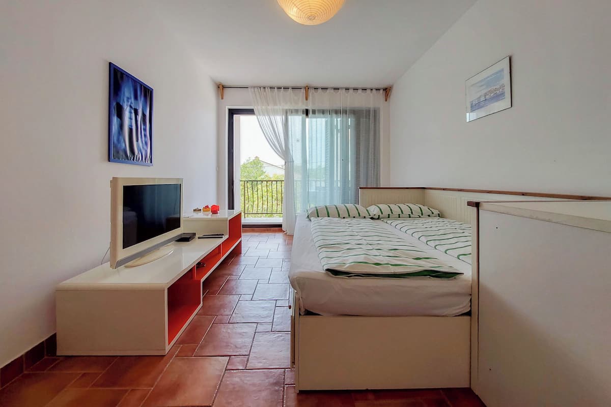 A bedroom with a bed, a TV, a small table, and a balcony with a view.