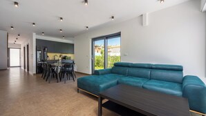 A modern living room with a teal sofa, a dark wooden coffee table, and a kitchen in the background. - House Neptunia (Medulin)