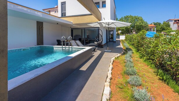 A modern outdoor pool area with a clear blue pool, a covered seating area, and a well-maintained garden. - House Neptunia (Medulin)