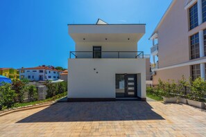A modern two-story building with a flat roof, a balcony on the upper floor, and a door with glass panels. - House Neptunia (Medulin)