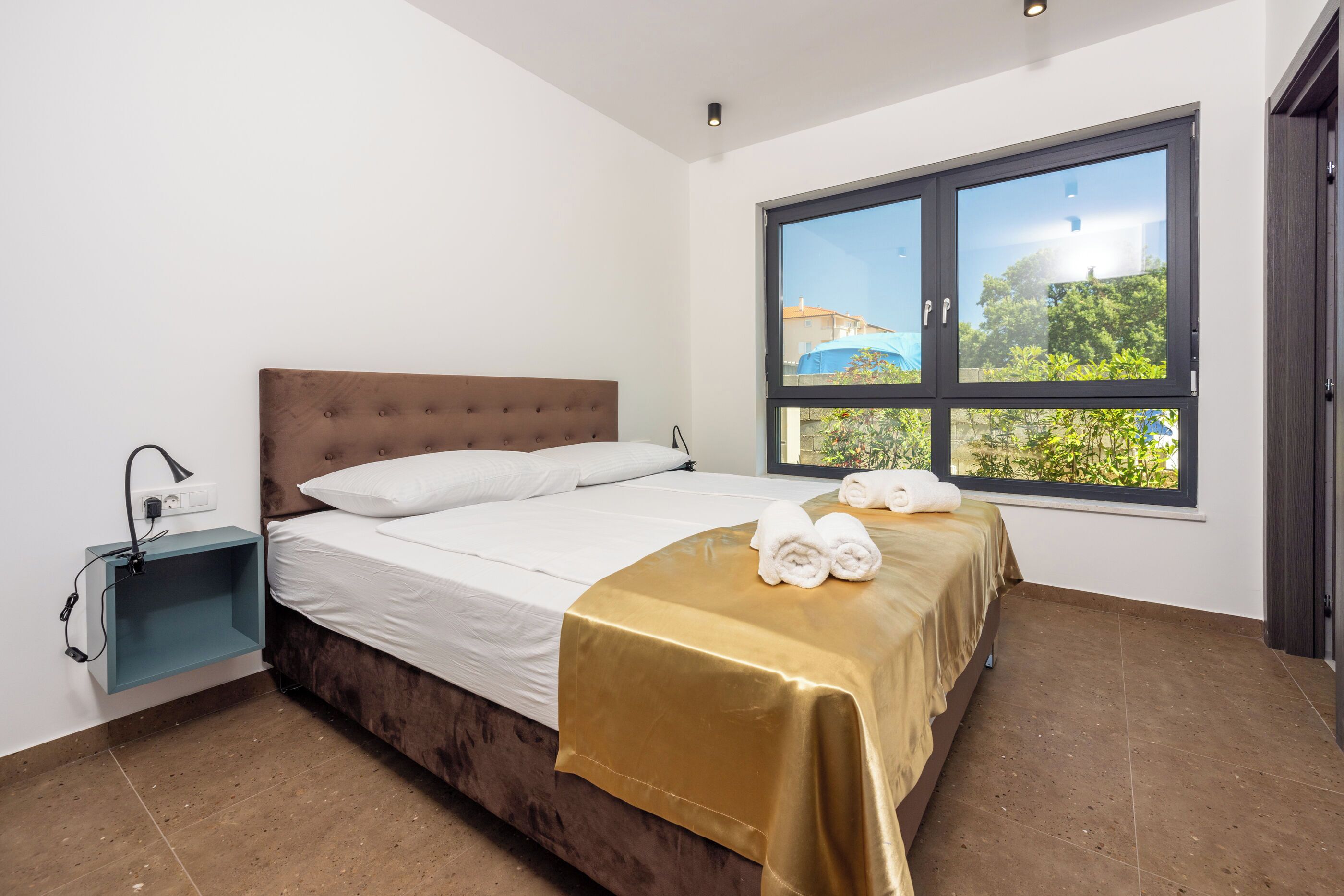 Un dormitorio con una cama, una ventana y una mesita de noche con lámpara.