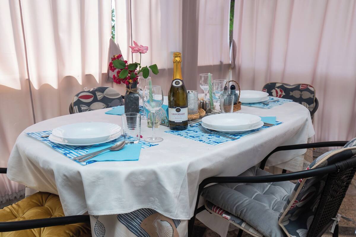 A round dining table with a white tablecloth, set with plates, cutlery, and a bottle of champagne.