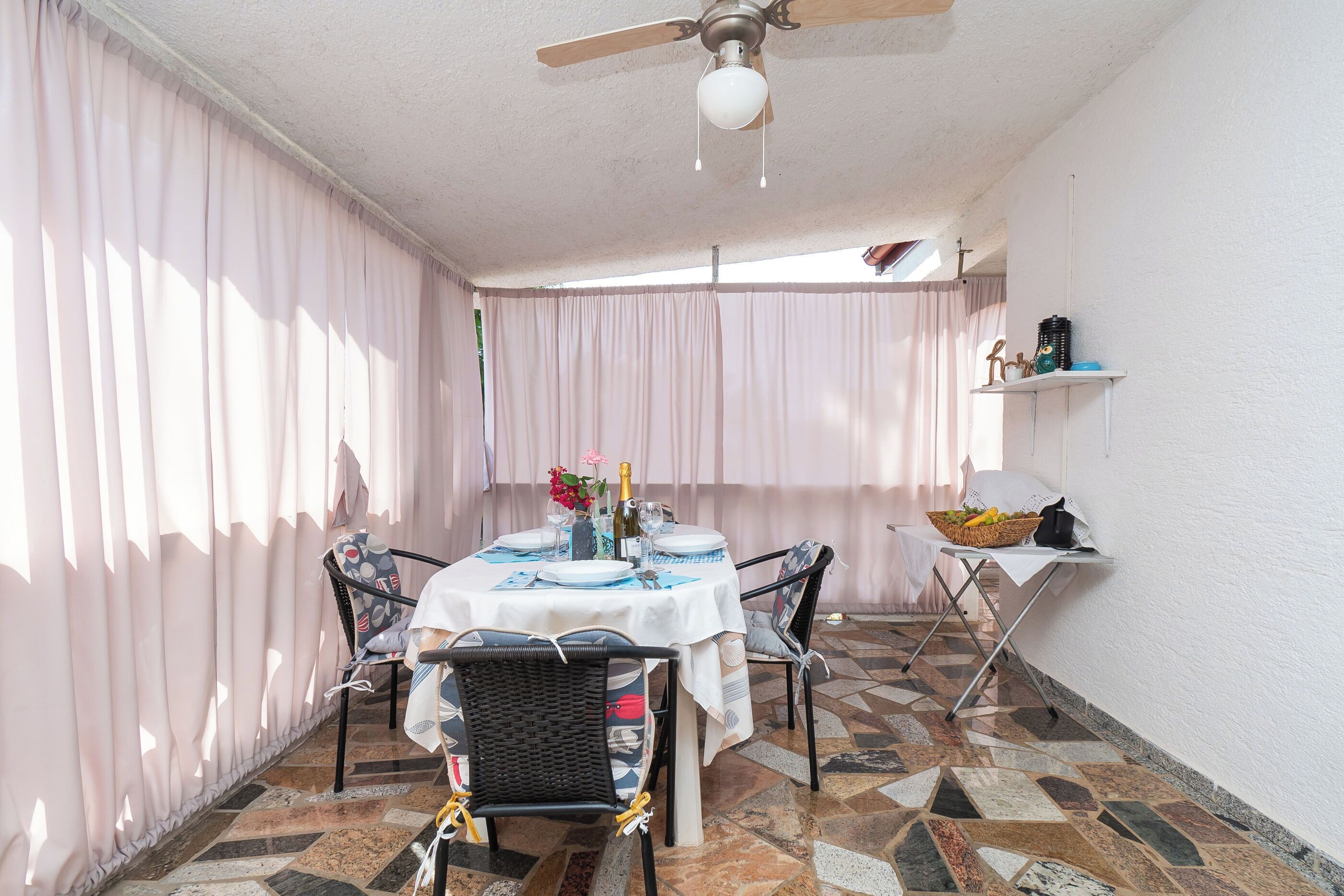 Uma sala de jantar com uma mesa redonda, cadeiras e um ventilador de teto.