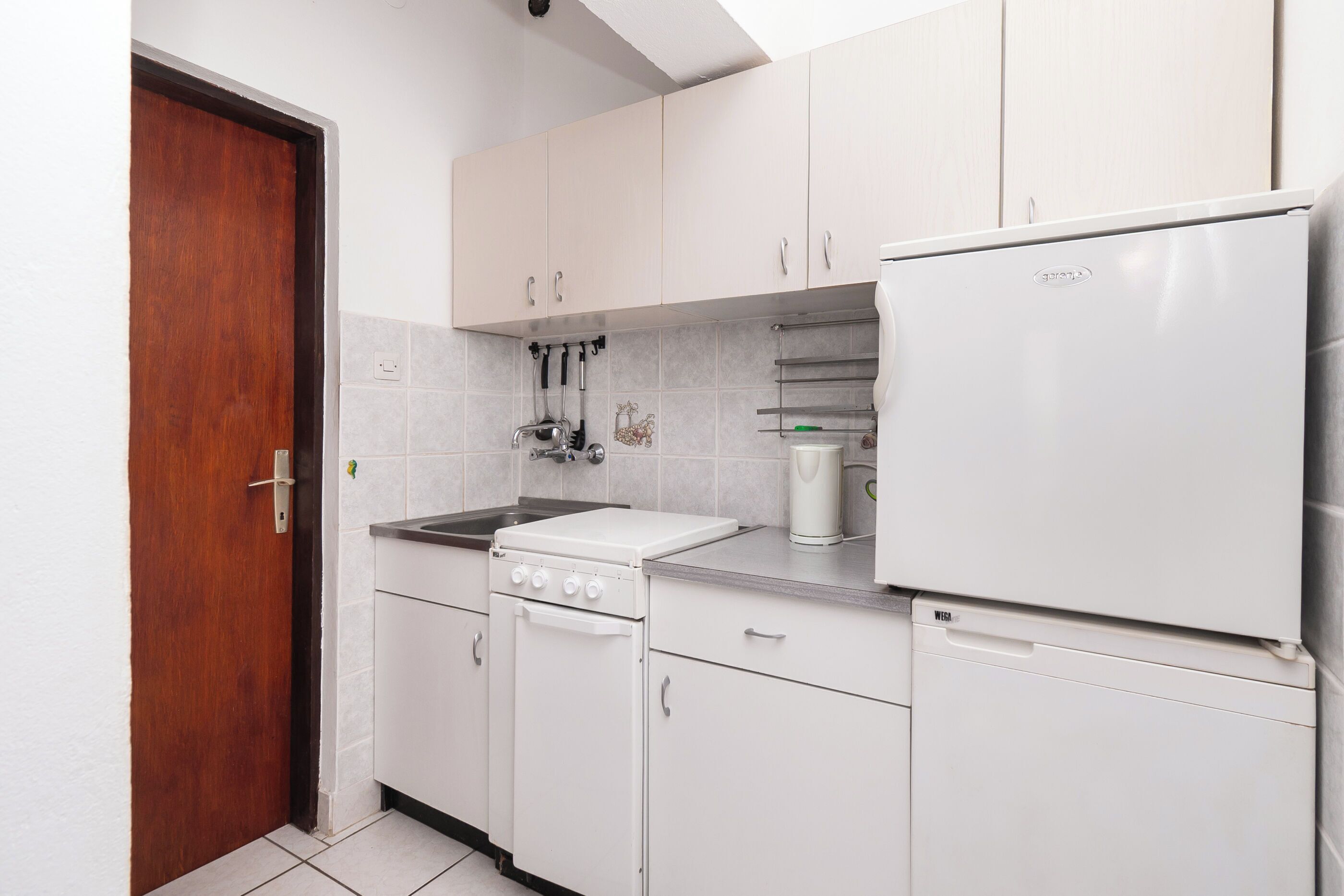 A kitchen with white cabinets, a stove, a sink, and a refrigerator.
