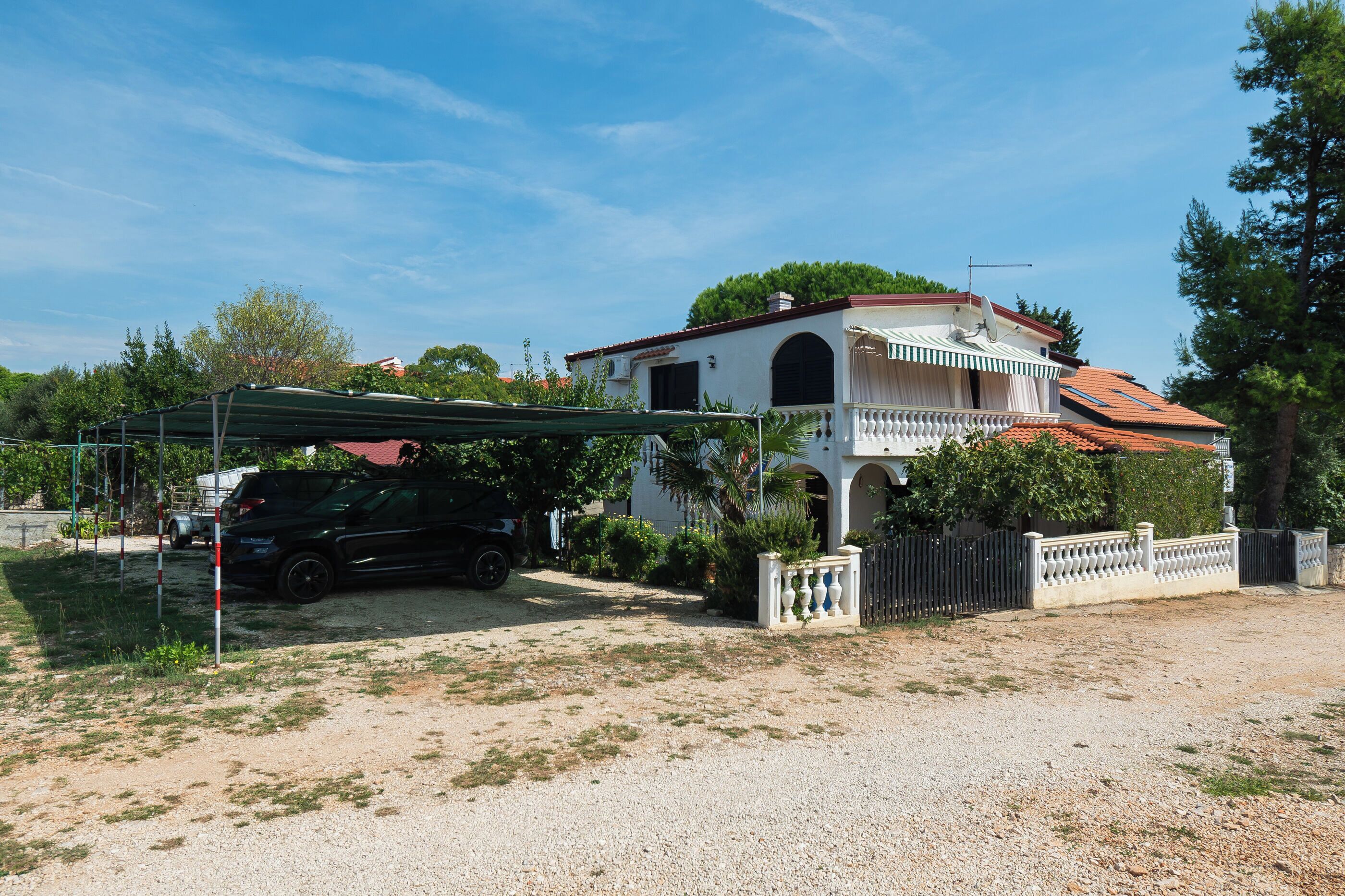 A two-story house with a red-tiled roof, a covered carport, and a gravel driveway.