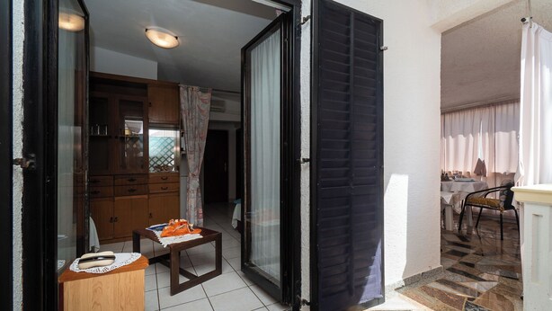 Una porta scorrevole aperta che dà su un'area pranzo con tavolo e sedie, una zona cucina con armadietti e un pavimento piastrellato.