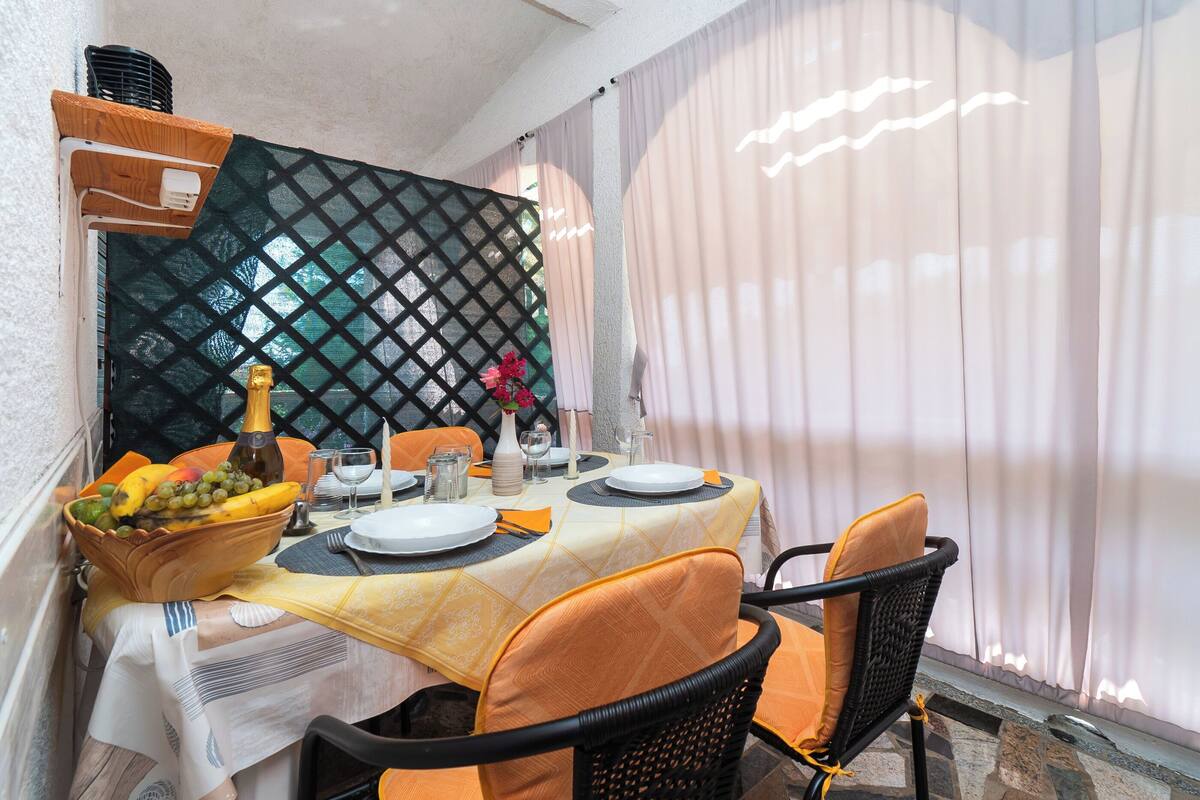 A dining area with a table set for four, featuring a fruit bowl, plates, and cutlery.
