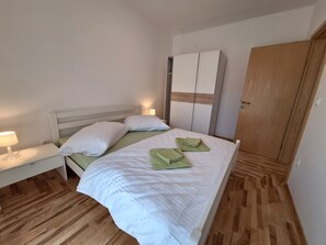 A neatly made bed with white linens and green towels, a bedside lamp, and a wooden wardrobe. - House Sanleon (Vinodol)