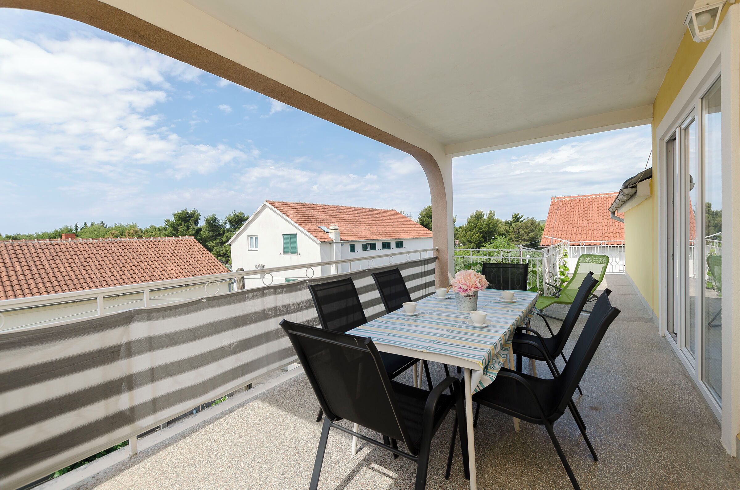 Un balcon avec une table et des chaises, une nappe à rayures et une vue sur des maisons aux toits rouges.