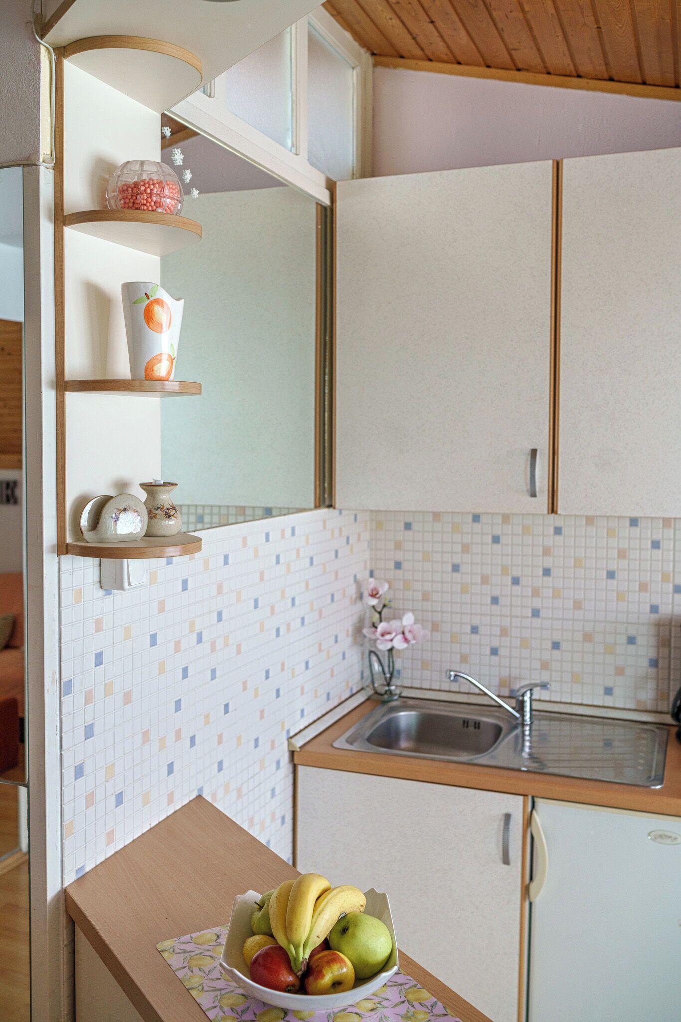 Une cuisine avec un plan de travail protégé par un revêtement mural en carreaux, un panier de fruits posé sur le comptoir et un évier.