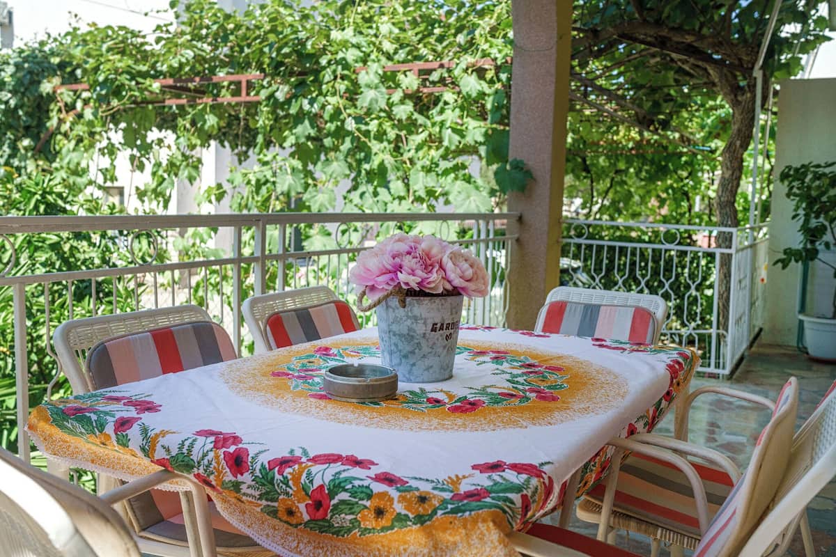 A round table with a floral tablecloth, surrounded by striped chairs, set on a balcony with a view of lush greenery.